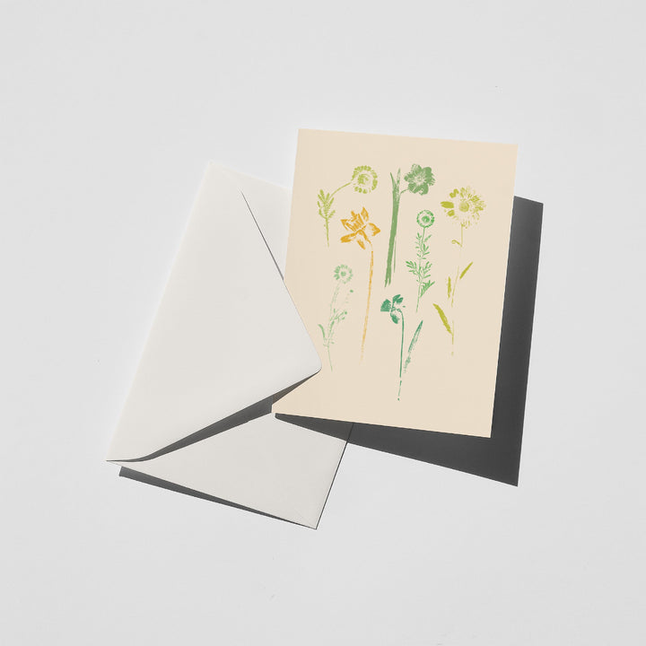 Greeting card with daisy and daffodil design and envelope on a light gray background