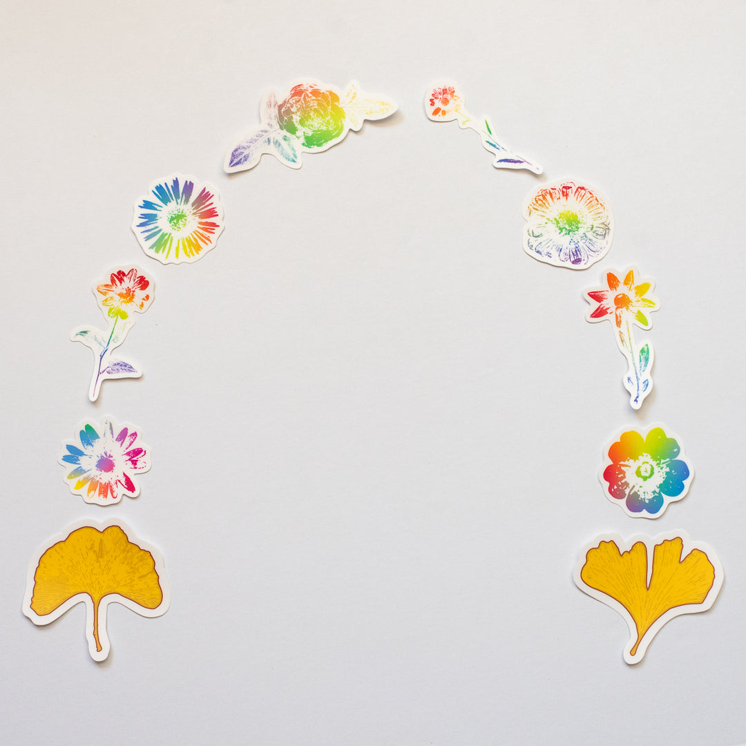 Colorful floral rainbow vinyl stickers in the shape of a horseshoe with two gold leaves at either end on a light gray background
