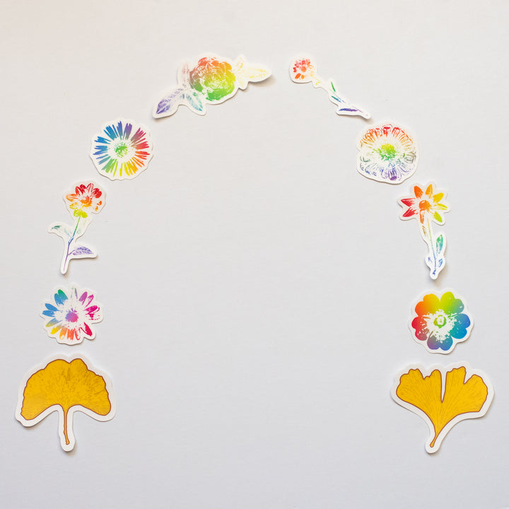 Colorful floral rainbow vinyl stickers in the shape of a horseshoe with two gold leaves at either end on a light gray background