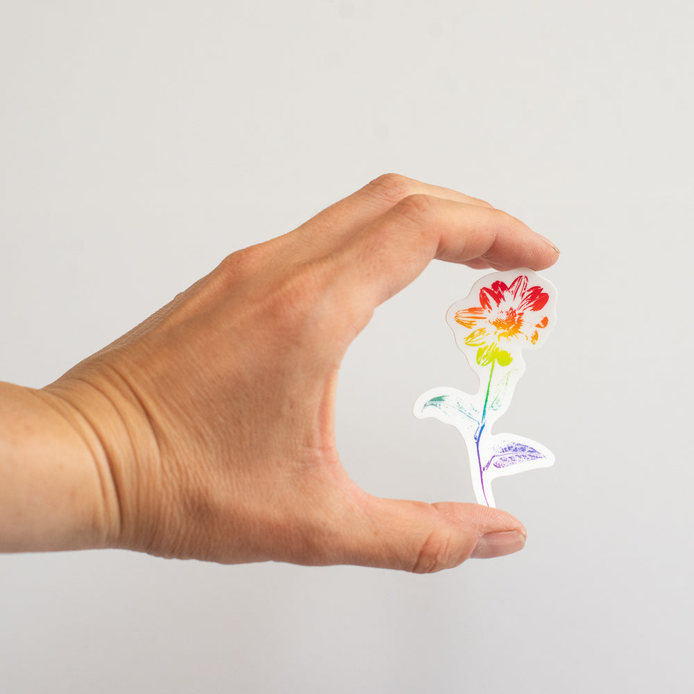 Hand holding a colorful flower-shaped sticker against a plain background