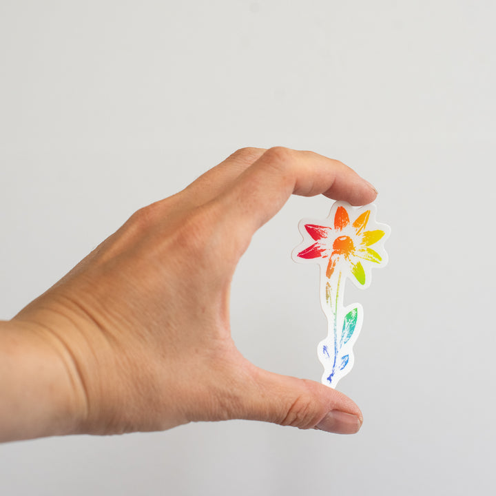 Hand holding a colorful flower-shaped sticker against a plain background