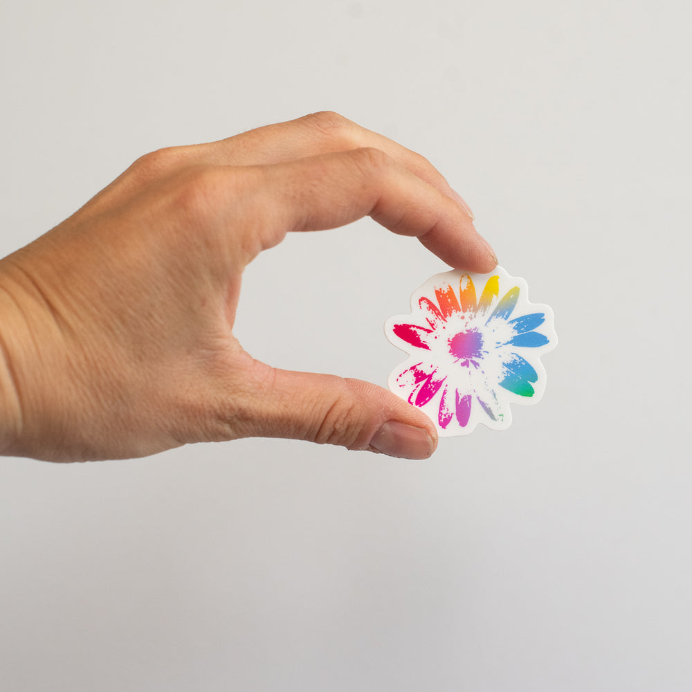 Hand holding a colorful flower-shaped sticker against a plain background