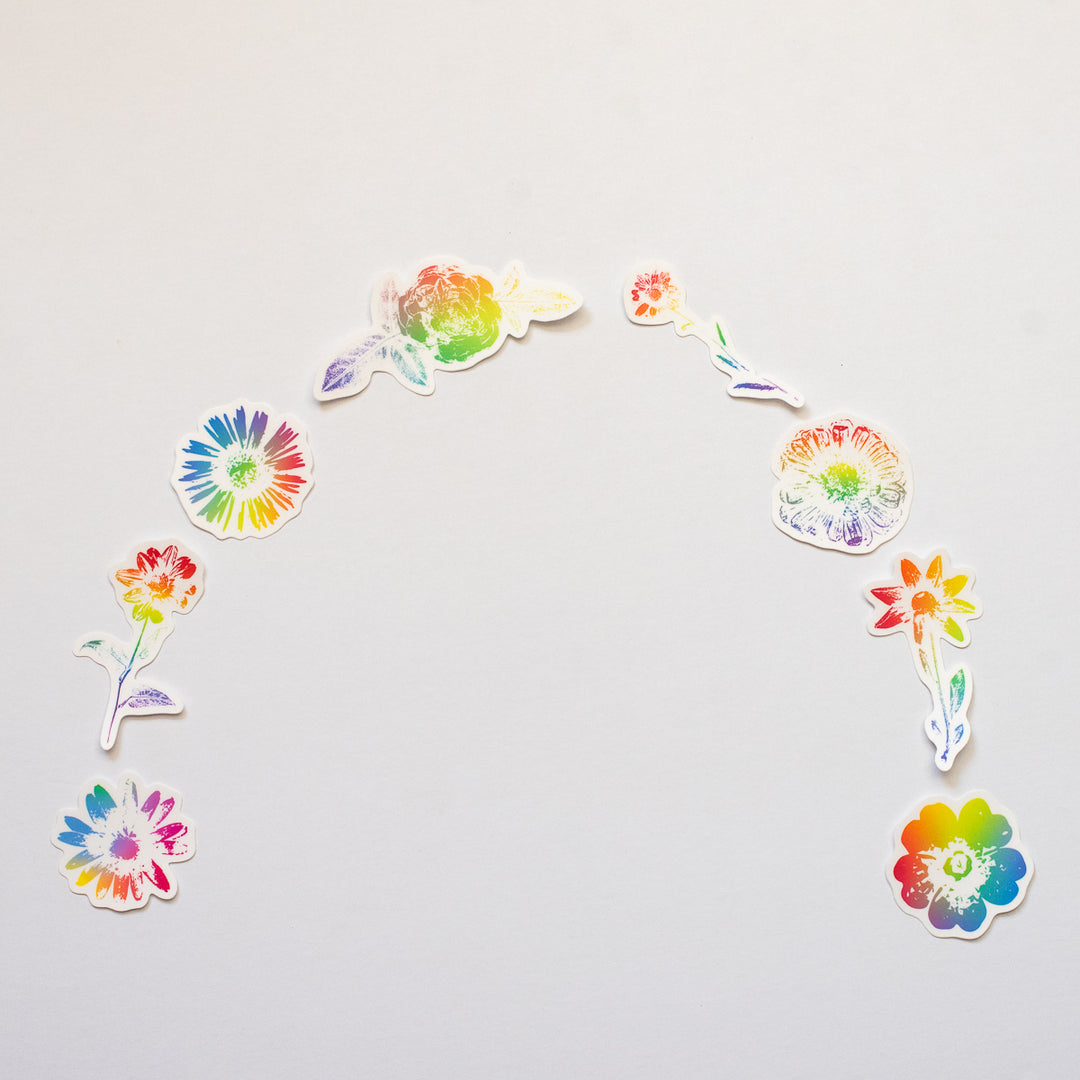 Colorful flower-shaped stickers arranged in a rainbow pattern on a light gray background.