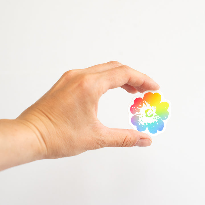 Hand holding a colorful rainbow flower-shaped sticker  against a white background