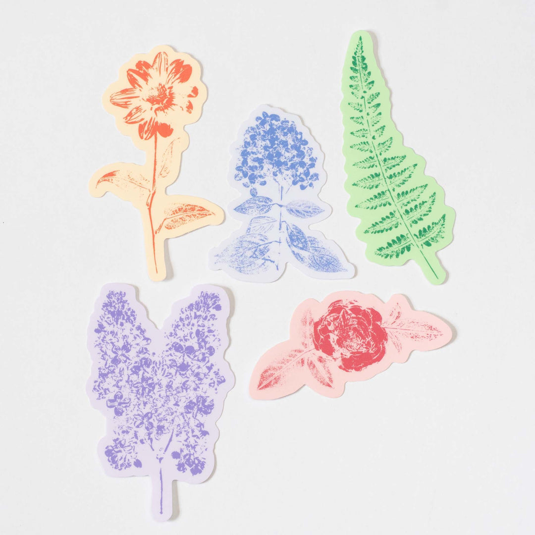 Five colorful floral and leaf-shaped stickers on a light gray background