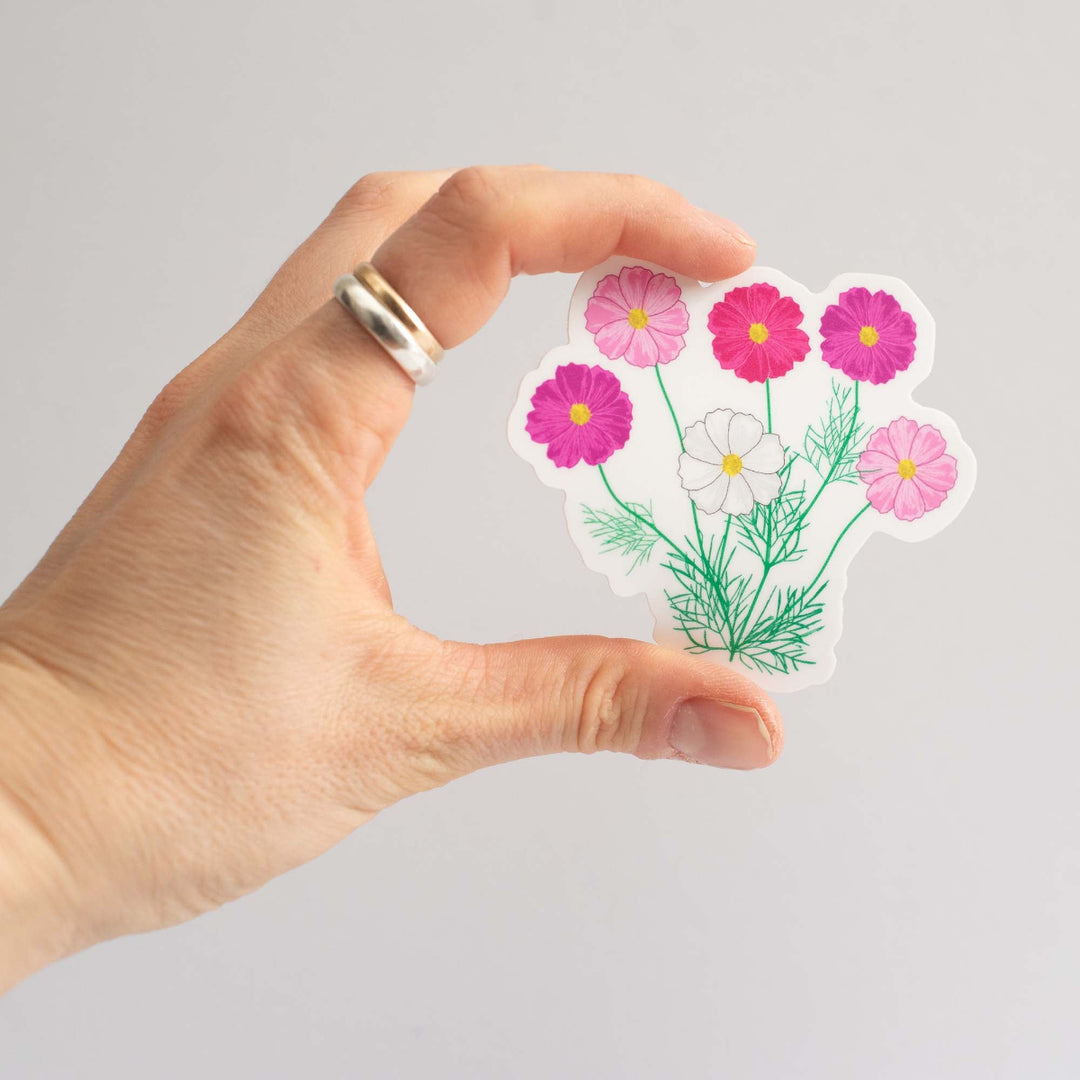 Hand holding a floral sticker with pink and white flowers on a gray background