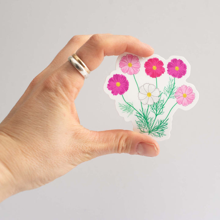 Hand holding a floral sticker with pink and white flowers on a gray background