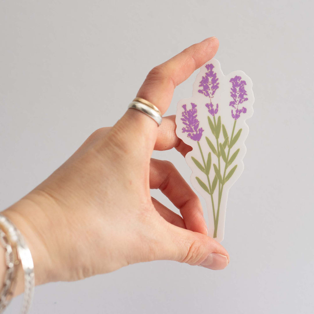 Hand holding a sticker with lavender designs on a light gray background