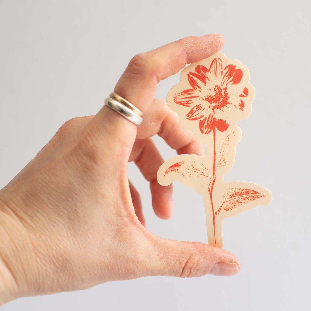 Hand holding an orange an peach sunflower floral cutout sticker against a plain background