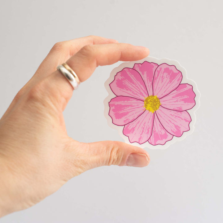 Hand holding a pink flower sticker against a light gray background